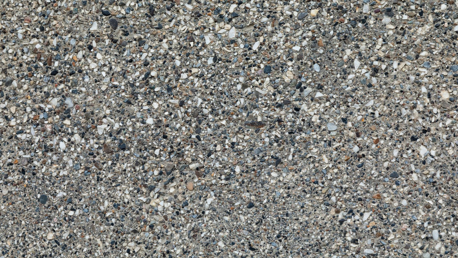 A flat close photograph of an exposed aggregate concrete surface, small grey, white and brown stones set in cement, filling the frame, with no text, people or setting in view.