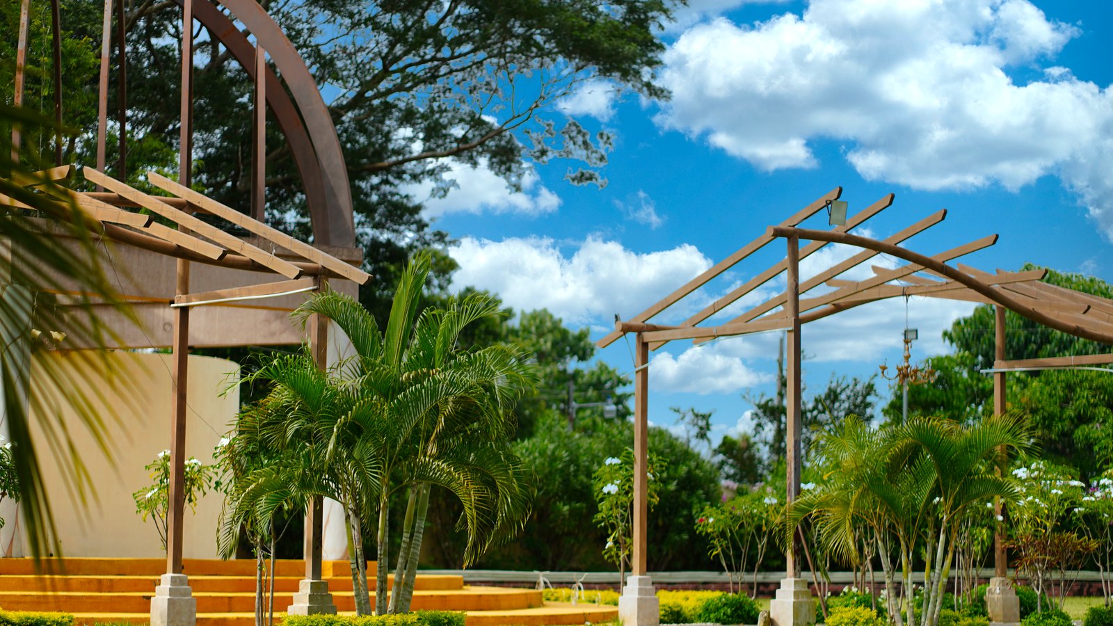 A tropical public garden has open lawn, palms and wooden pavilion structures. Stock photo, not Mike Greenwell Regional Park.