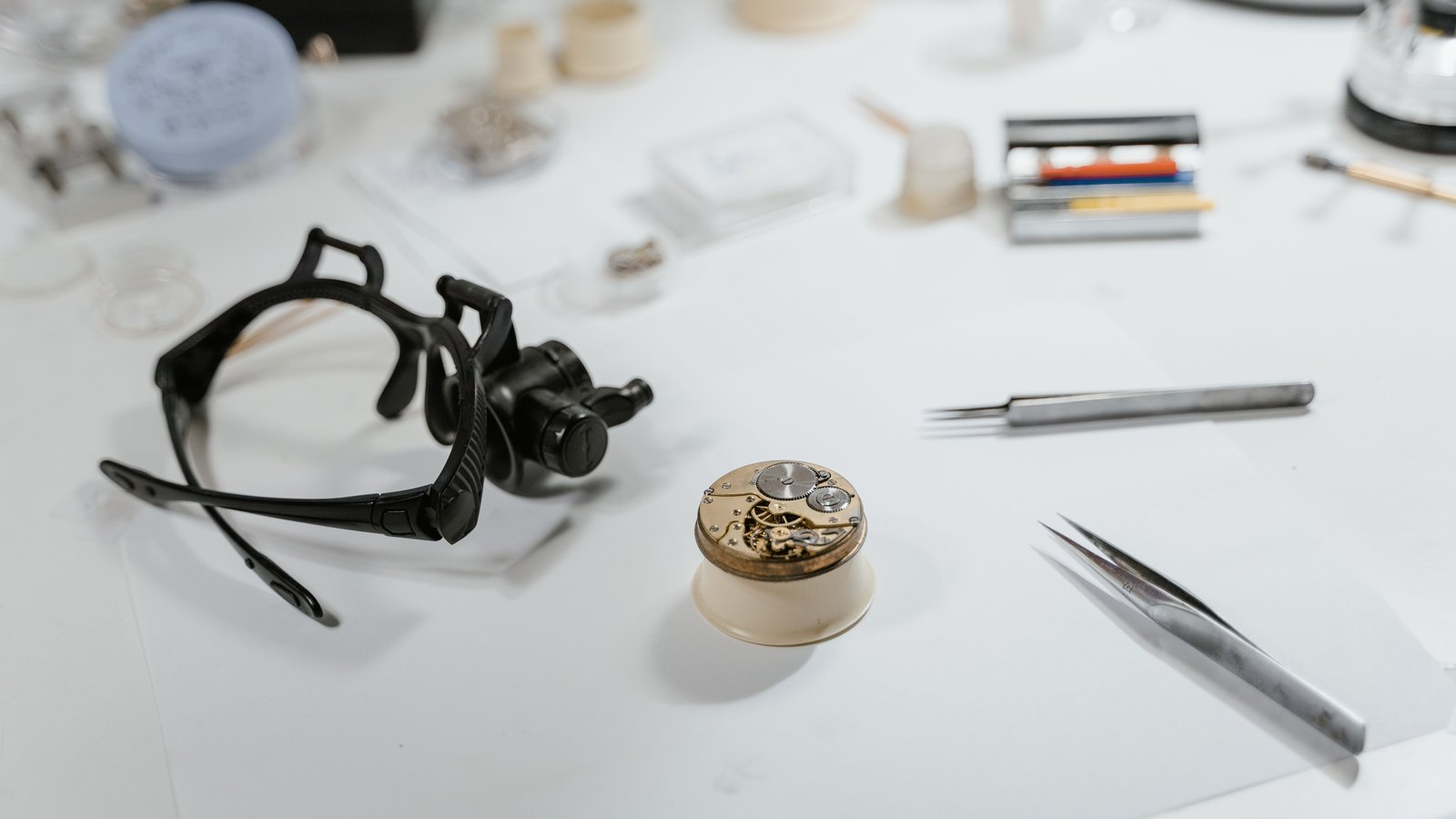 A mechanical watch movement rests among a loupe and watchmaking tools.