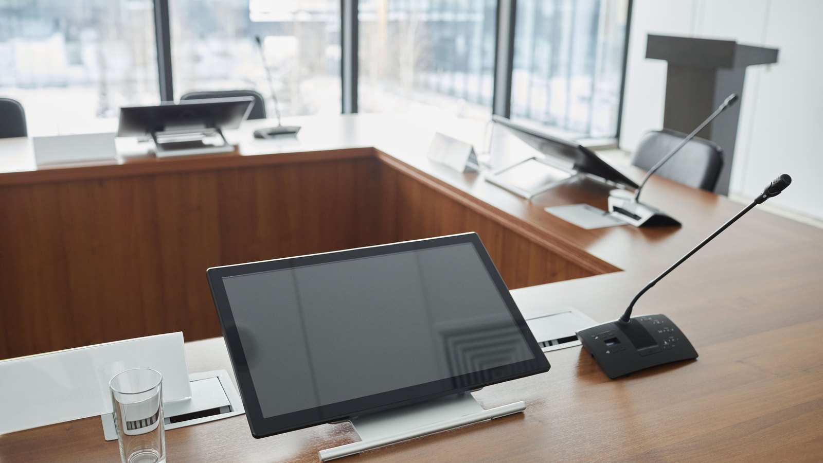 An empty meeting chamber with microphones and blank desk screens, not a photograph of the River Park East project.