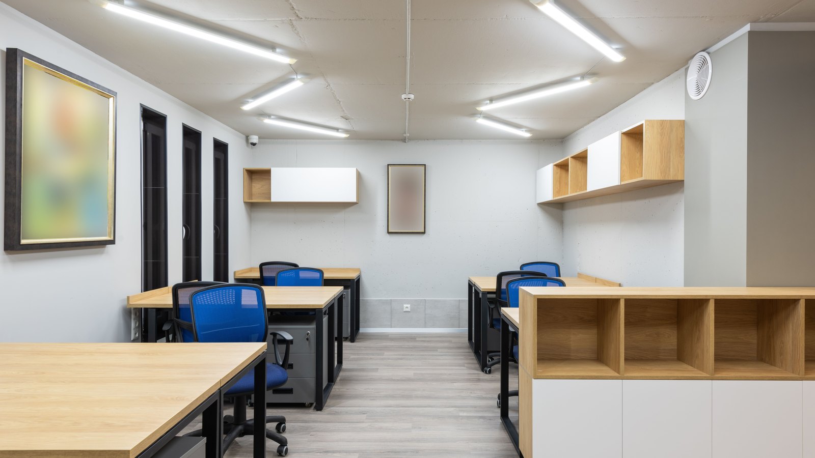 An empty modern office with rows of desks and blue chairs.