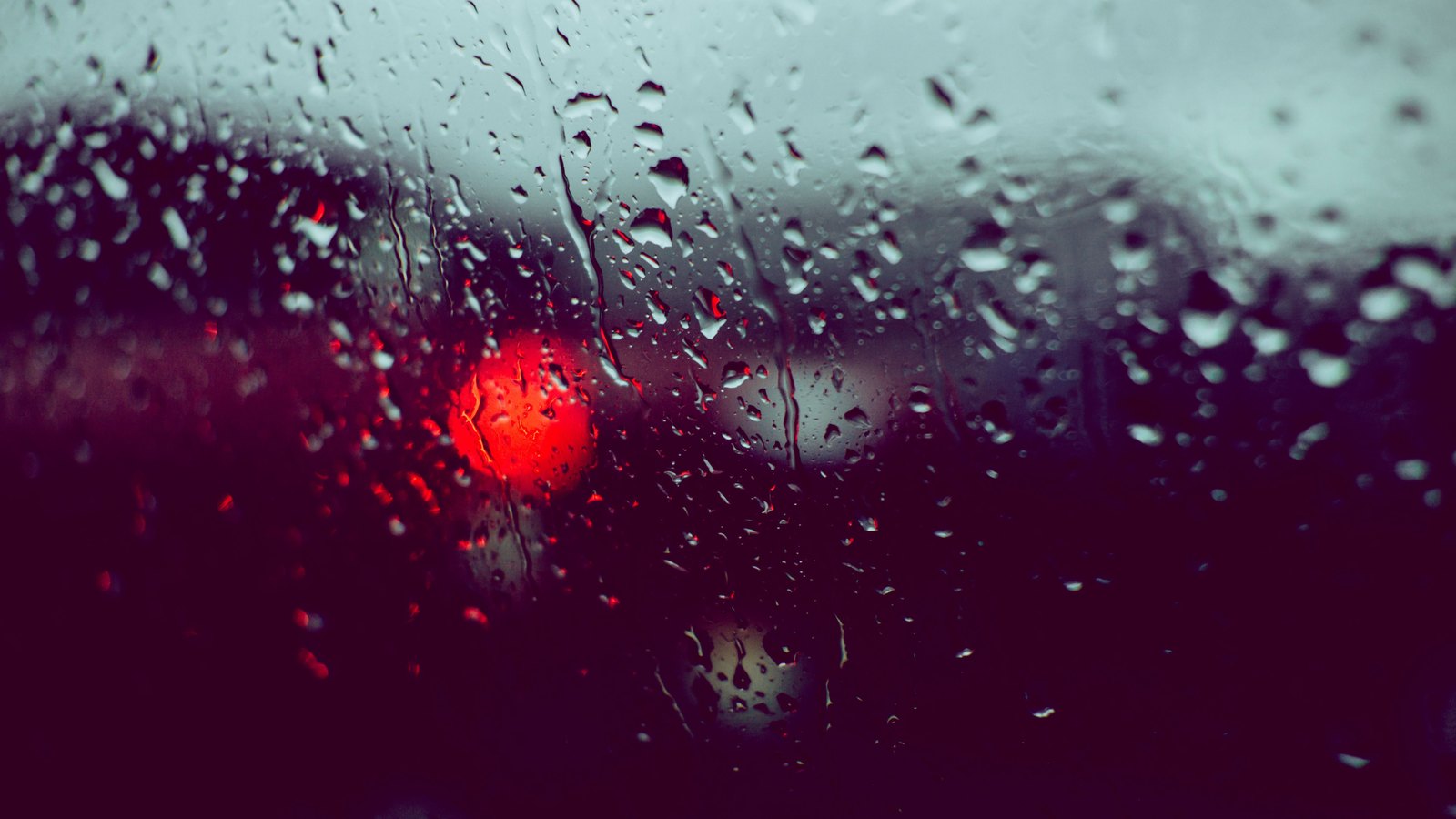 Rain beads on a car window while traffic lights blur beyond it, not a photograph of this advisory.