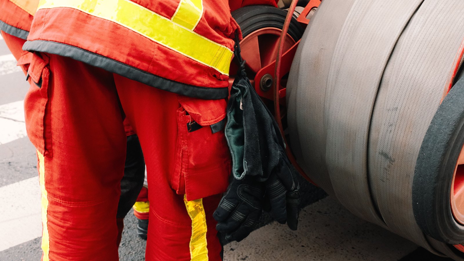 Firefighters in red protective gear beside a hose reel, not a photograph of this event.