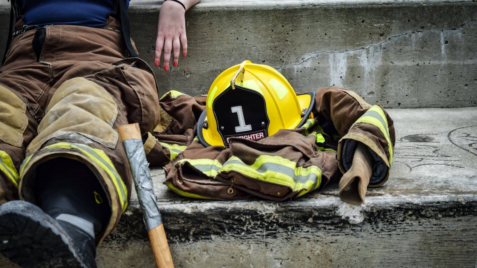 A firefighter rests beside turnout gear and a yellow helmet, not a photograph of this event.