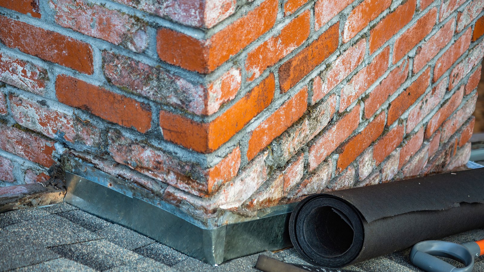 Roofing membrane and hand tools beside a brick chimney, not a photograph of this event.