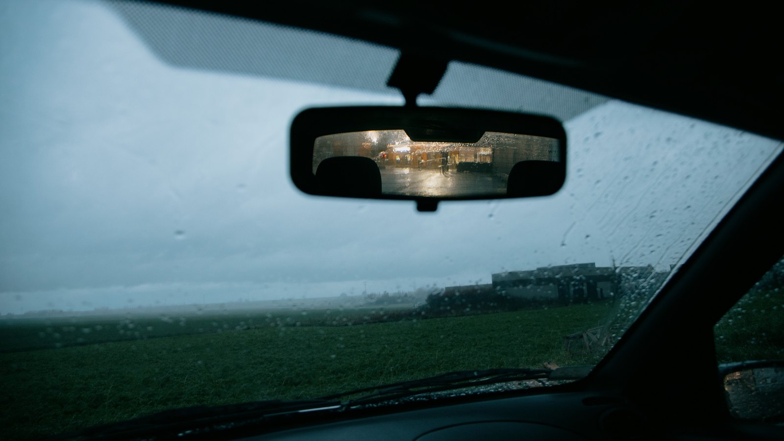 Heavy rain seen through a car windshield over flat green ground, not a photograph of this event.