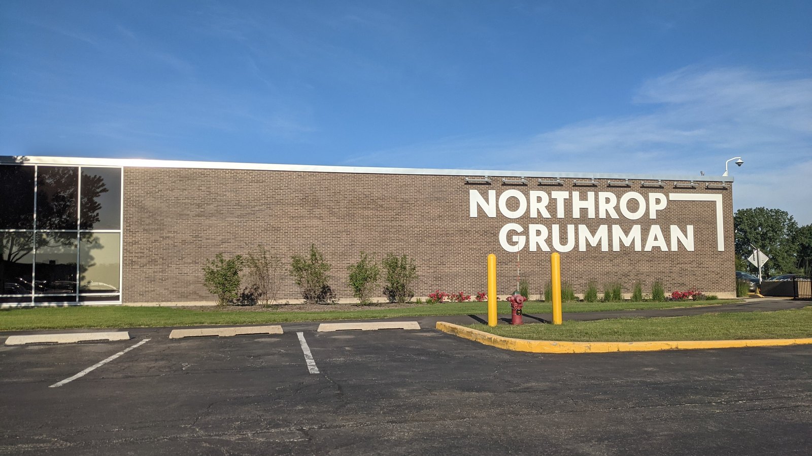 A long single storey brick office building in Rolling Meadows, Illinois with the Northrop Grumman name in white lettering across one end, seen from an empty stretch of its car park under a clear sky.