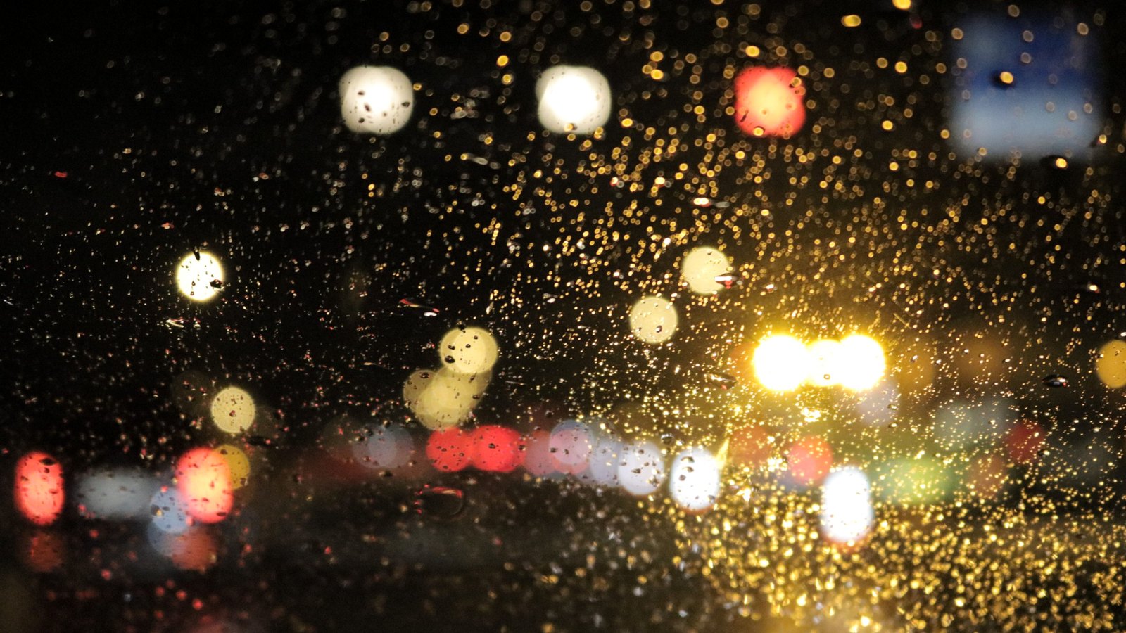Rain beads on a windshield as lights blur on a dark street, not a photograph of this event.