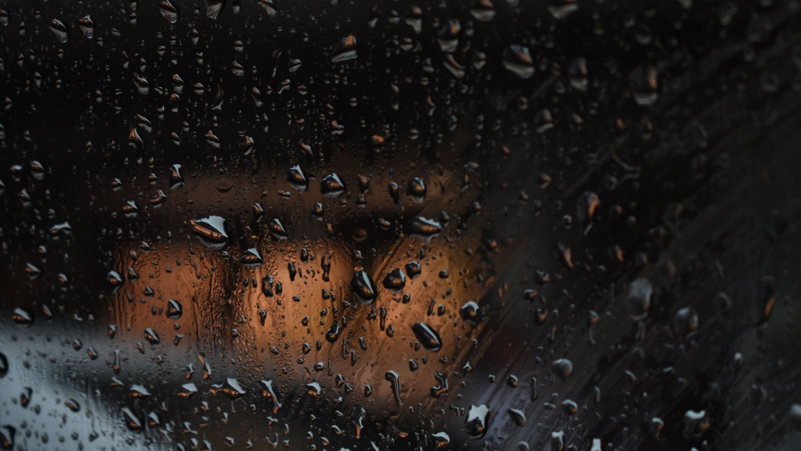 Rain beads on glass blur amber lights beyond it, not a photograph of this advisory.