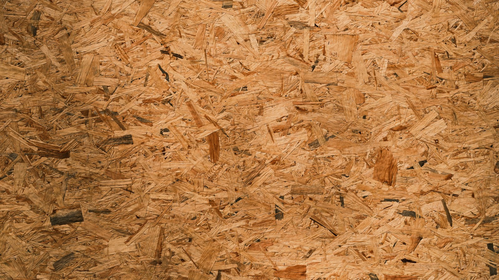 A close photograph of a pressed board of wood strands, pale orange flakes lying at every angle and packed flat across the whole frame. No object, person, lettering or brand mark is visible.