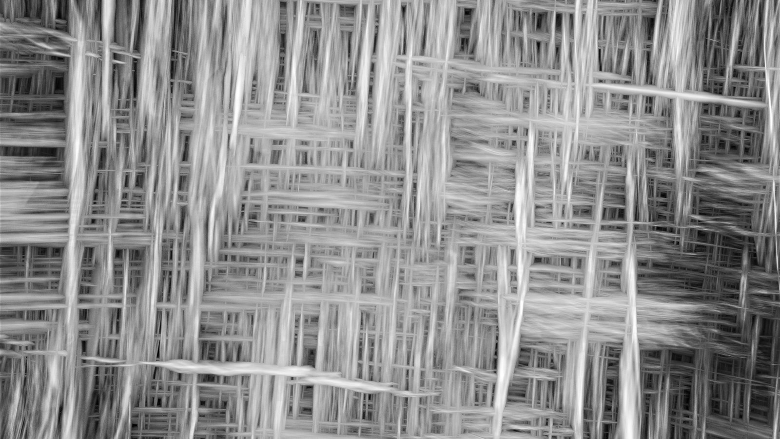 A close monochrome photograph of a woven texture filling the whole frame, pale threads crossing at right angles in a dense grid, with longer streaks of light drawn vertically across the surface so that parts of the weave appear smeared and blurred.