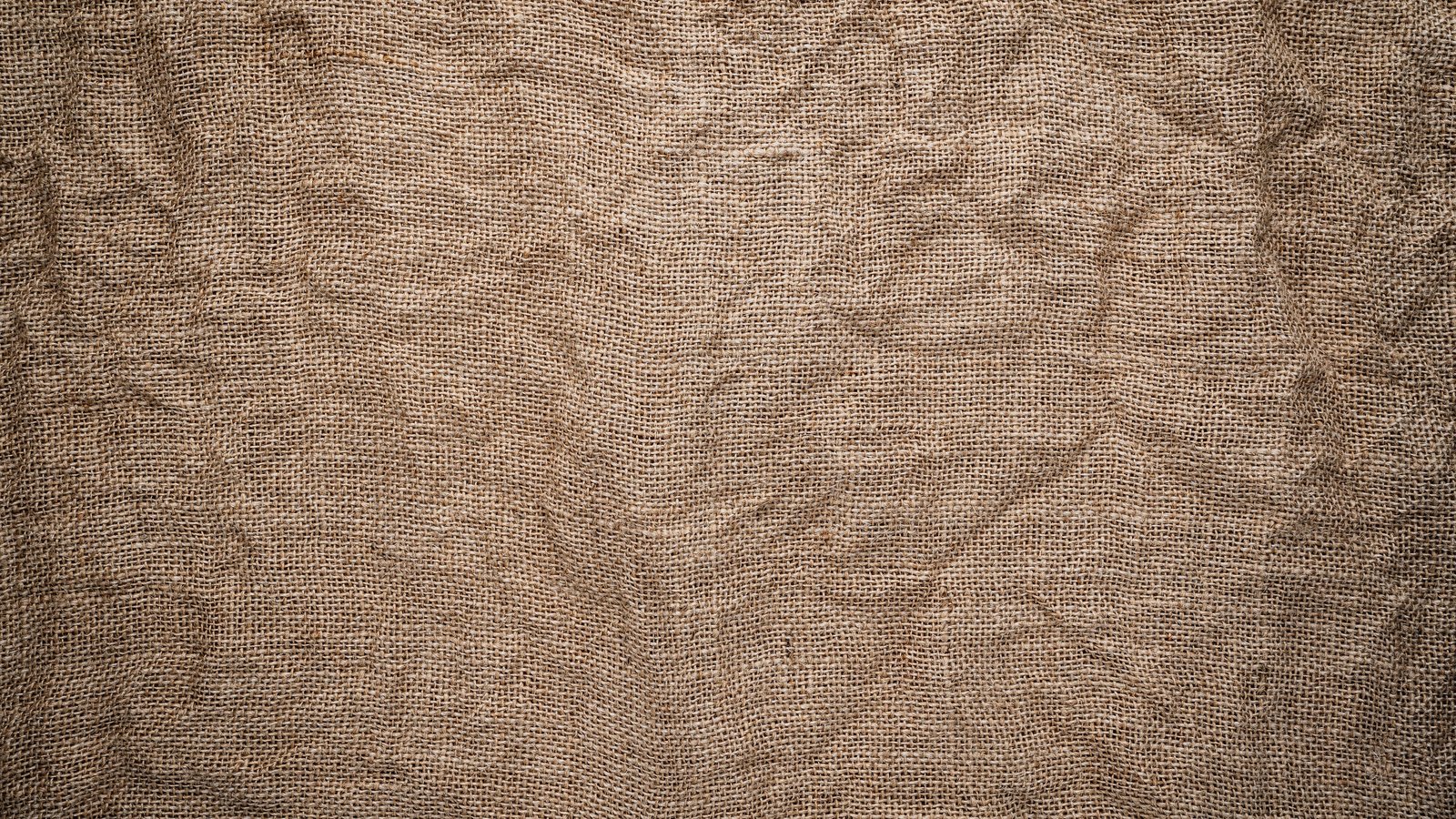 A close photograph of coarse brown burlap sacking filling the frame, its open jute weave lightly creased and lit evenly, carrying no printing, stencilling or markings of any kind.