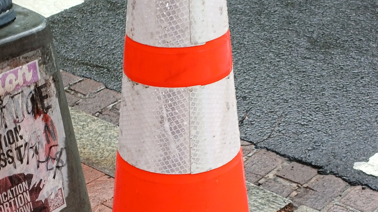 A close-up of an orange traffic cone beside a city street, not a photograph of this closure.