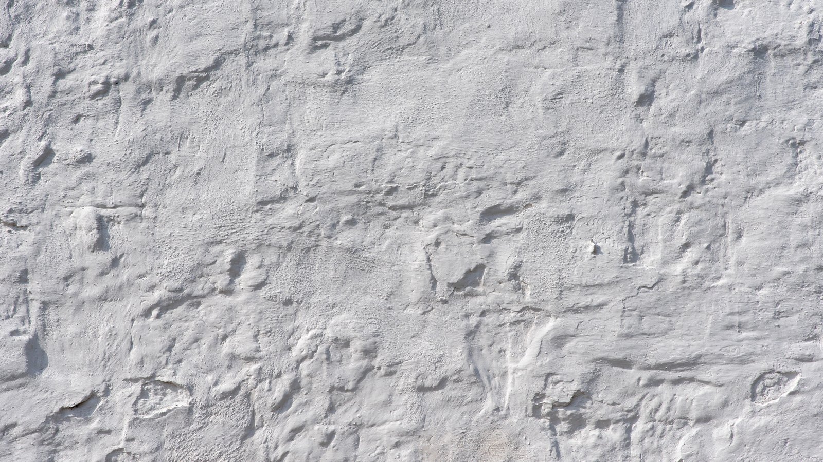A white rendered wall photographed square on and filling the frame. The surface is uneven, with trowel ridges, shallow hollows and small pocks throwing faint grey shadows across an otherwise plain white finish. No lettering, markings or fixtures are visible.