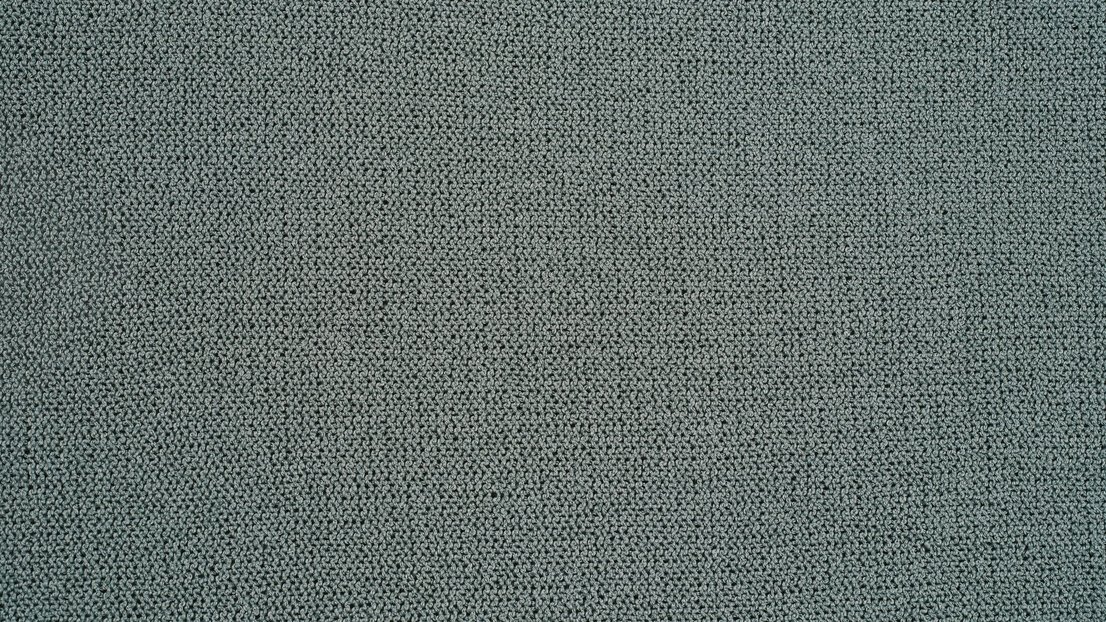 A close overhead crop of a fine gauge knitted fabric in muted grey green, the loops running in even rows across the whole frame with slight shifts of shade from one band to the next. No text, brand mark, person or place is in view.