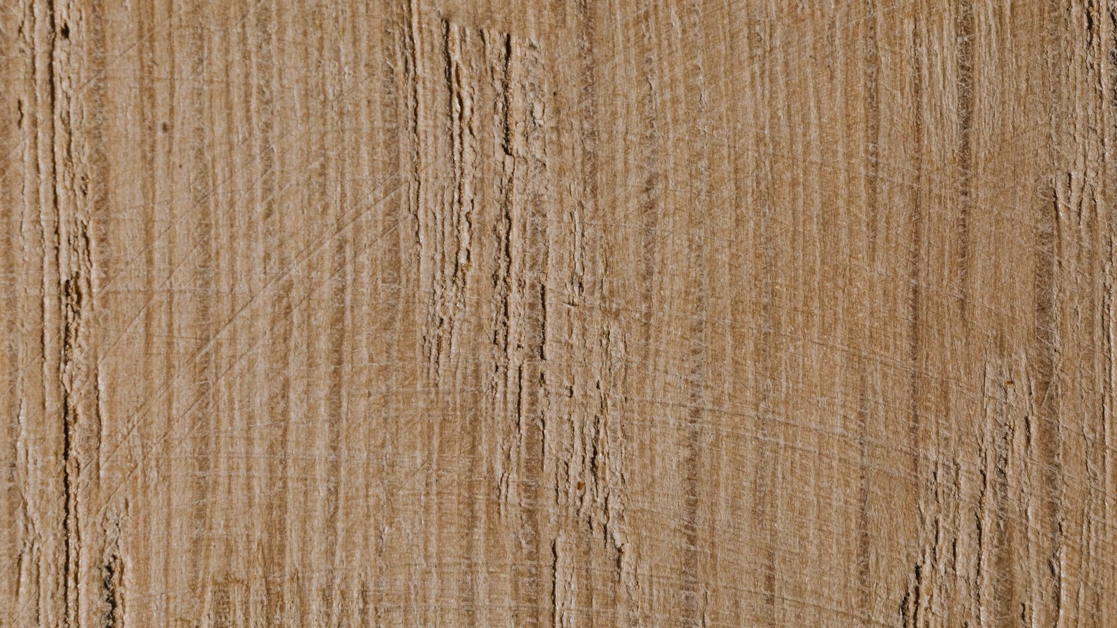 A close photograph of a sawn board of pale tan timber filling the frame, the vertical grain broken by saw marks running diagonally across it, with no object, marking or lettering in the picture.