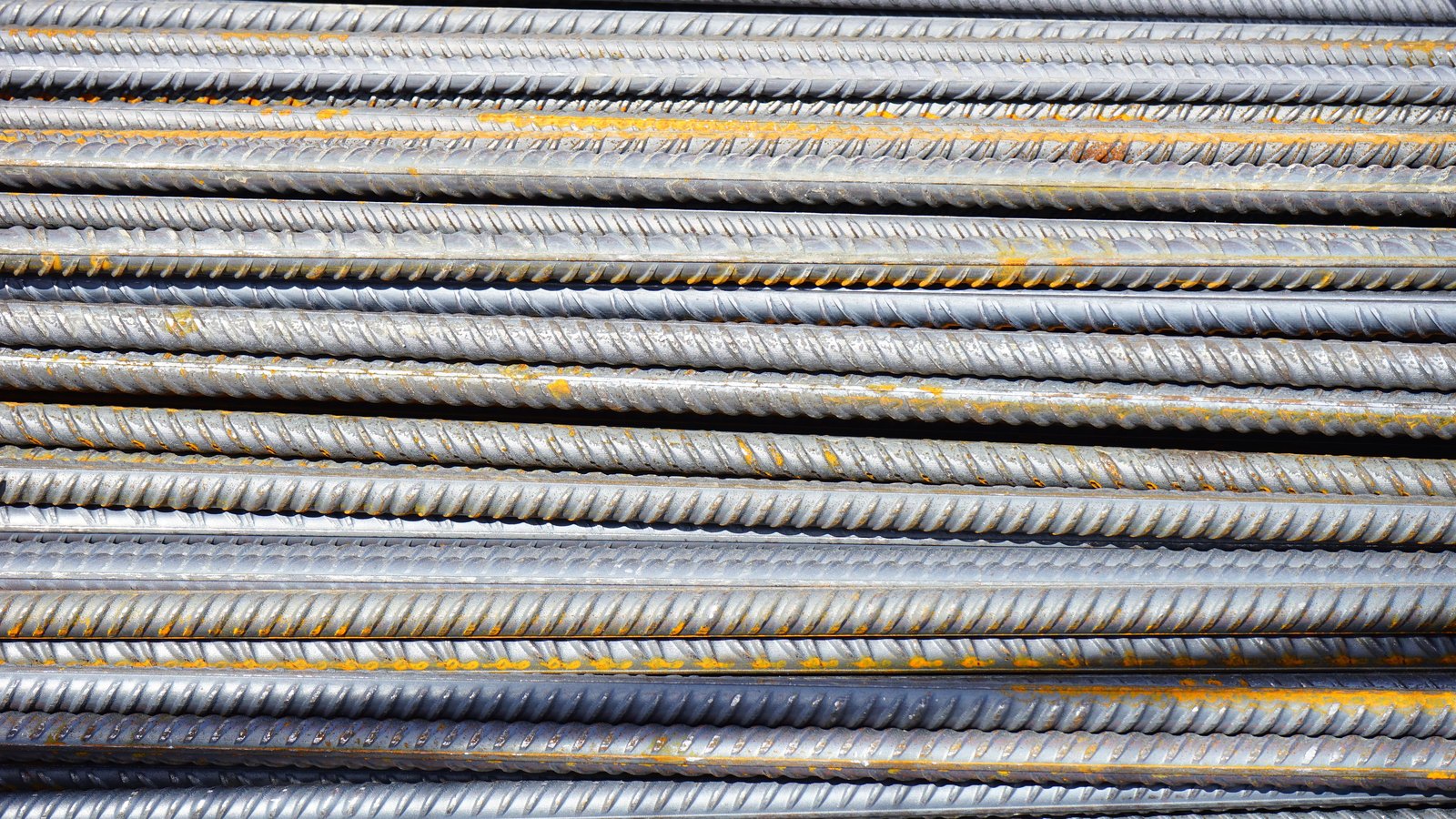 A stack of deformed steel reinforcing bars lying parallel across the frame, their ribbed surfaces grey with patches of orange surface rust.