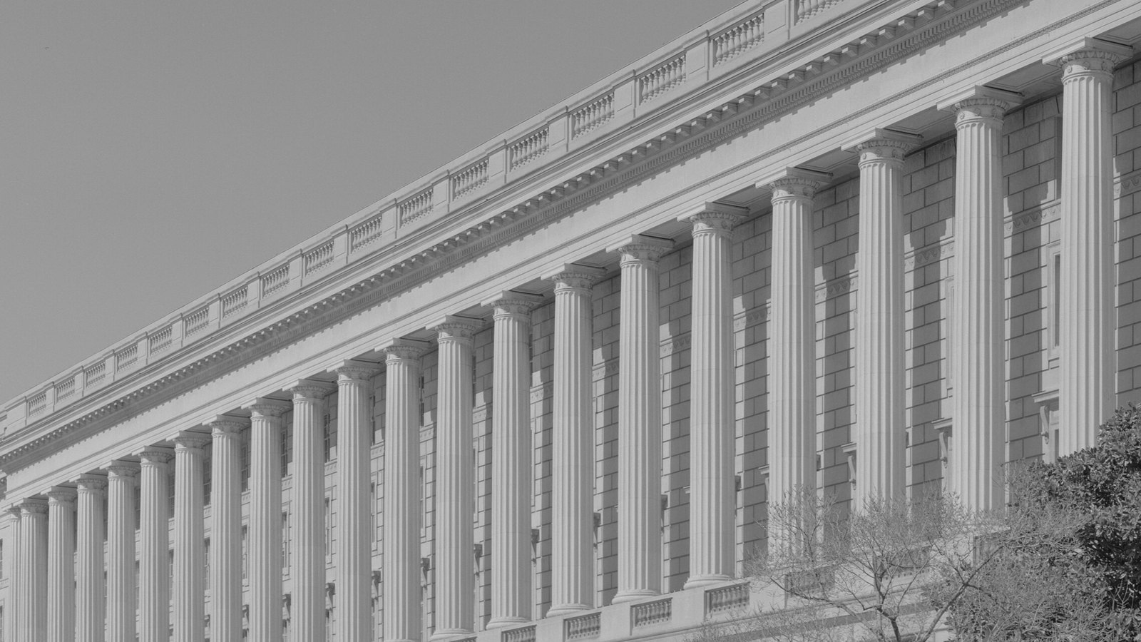 The upper facade of the Internal Revenue Service headquarters in Washington, a long row of fluted stone columns receding along Constitution Avenue against a plain sky.