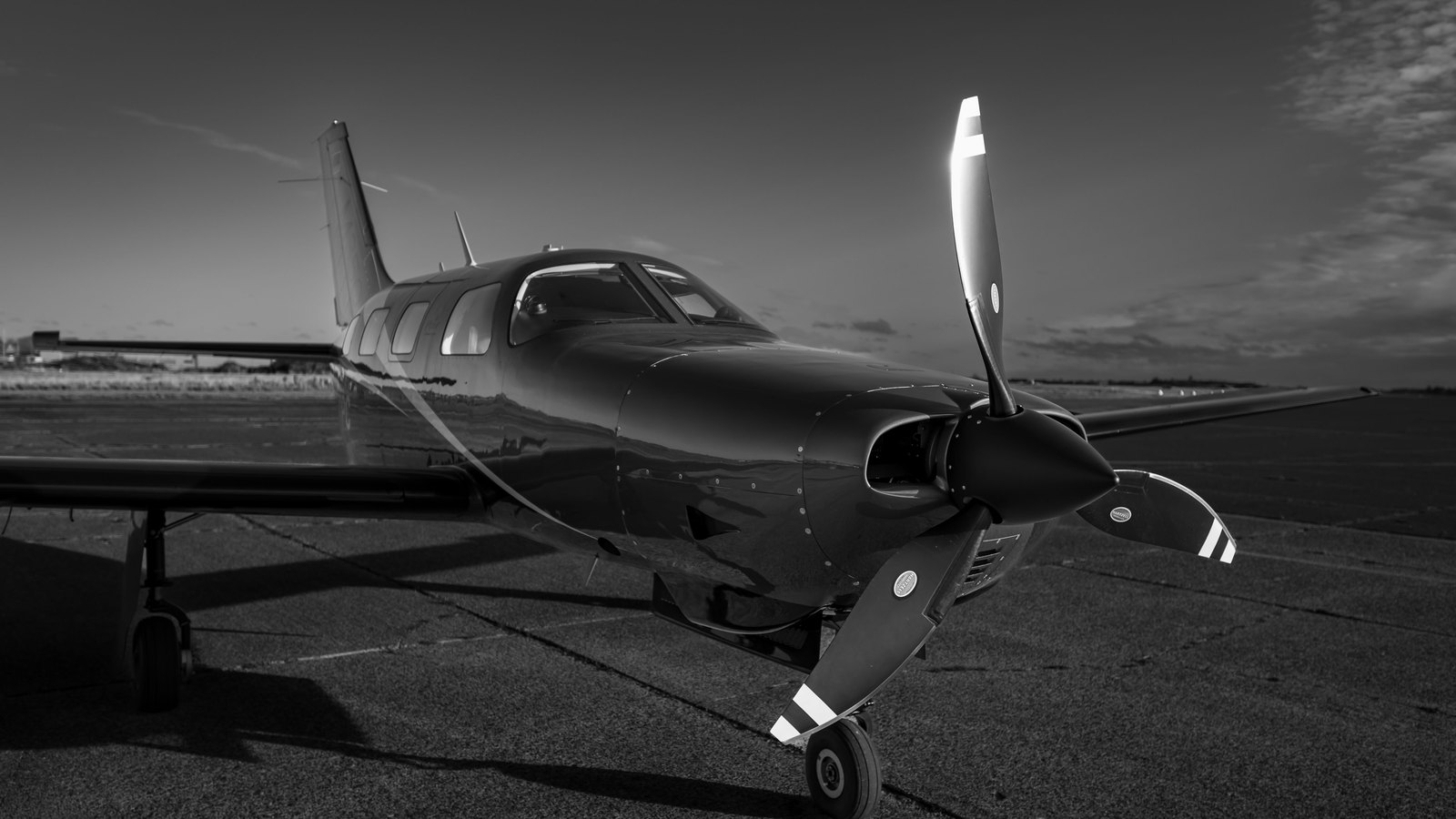 A single engine low wing propeller aeroplane parked on a flat airfield apron under an open sky, photographed in black and white from the front quarter with the propeller standing upright, and no people, registration marks, signage, text, logos or identifiable location anywhere in the frame. A generic illustration of a light aircraft, not a photograph of the aeroplane in this story.