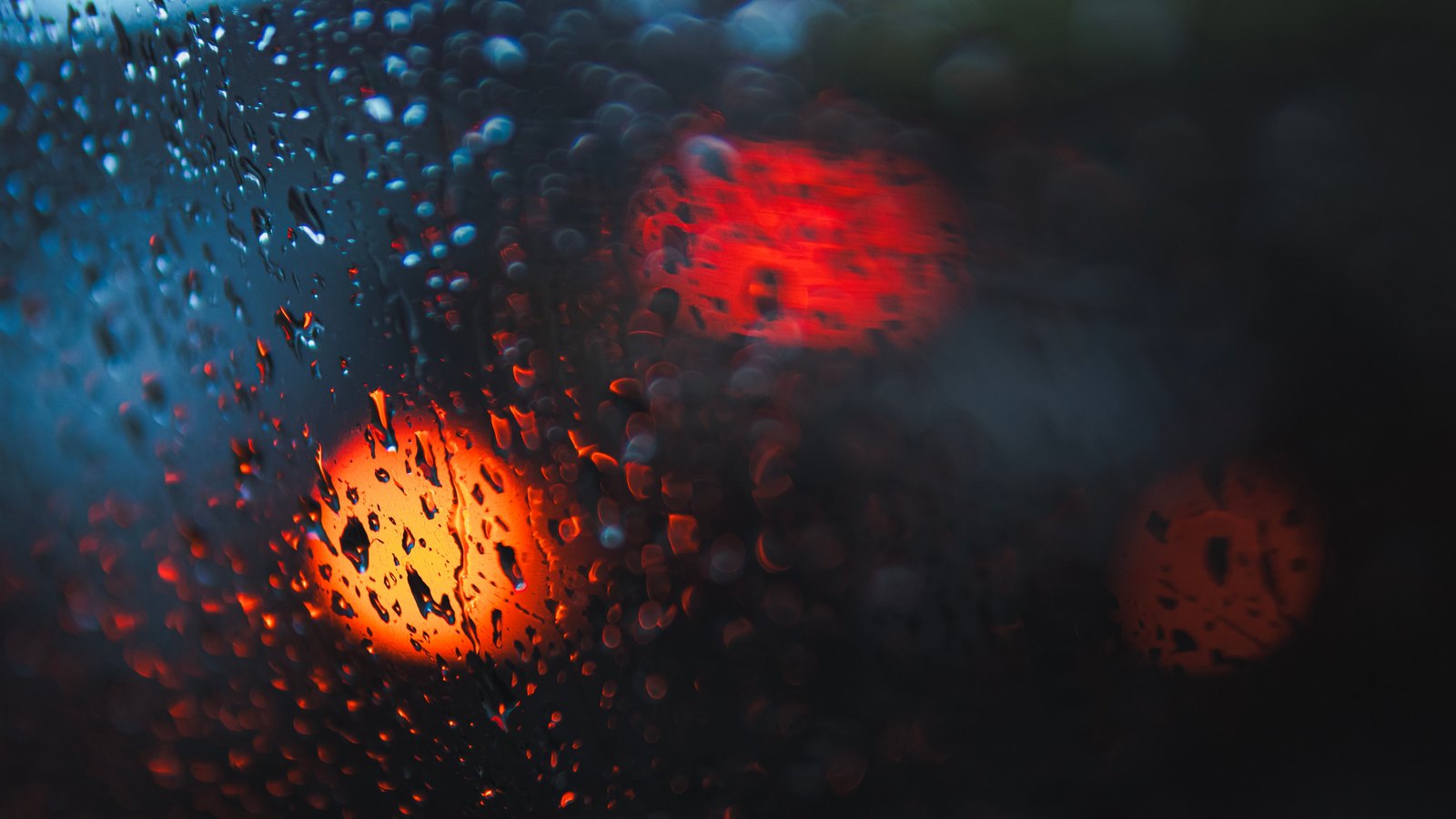 Red and blue emergency lights blur through raindrops on glass against a dark background, with no people, vehicles, signs or location visible. This is a stock photograph and not the actual scene.