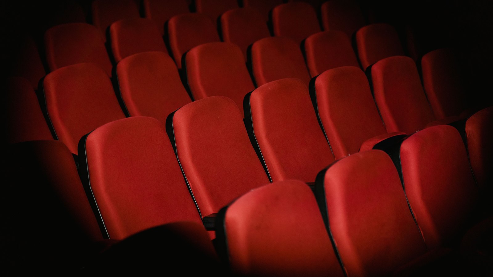 Rows of empty red upholstered seats in a darkened movie theater.