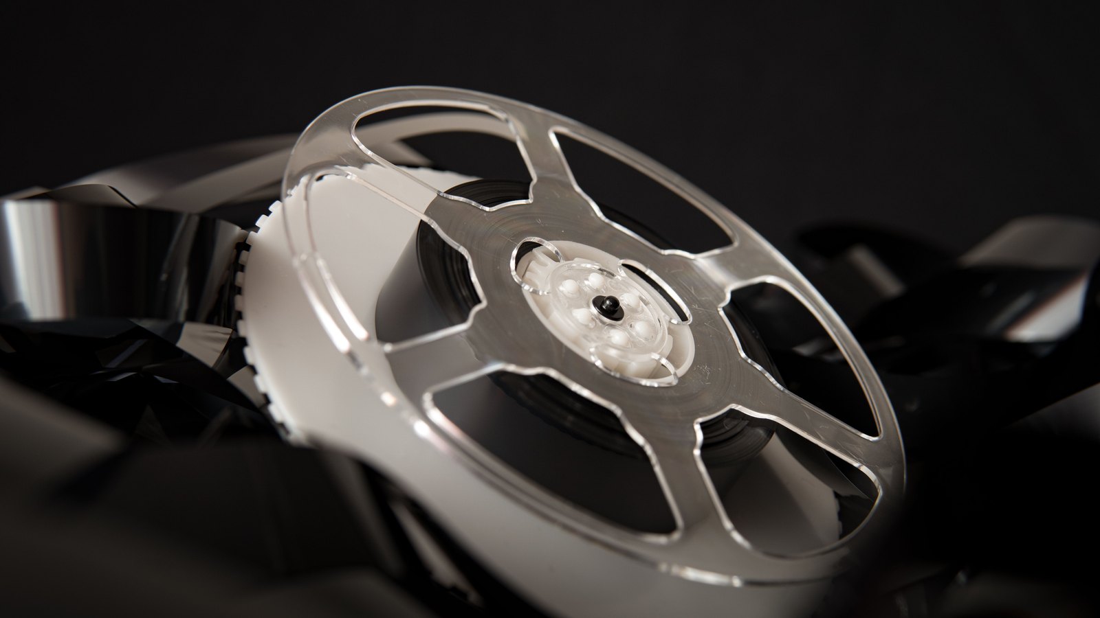 A metal reel wound with film, resting on a loose heap of film against a black background.