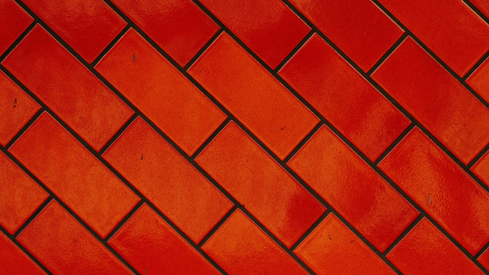 Glazed red rectangular tiles laid in a diagonal herringbone pattern, photographed flat and filling the whole frame, with dark grout lines between them and slight variation in the glaze. No text, sky or object edge is visible.