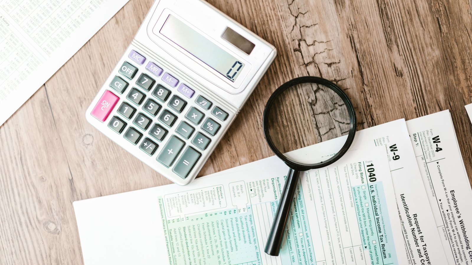 A calculator and magnifying glass resting on financial forms.