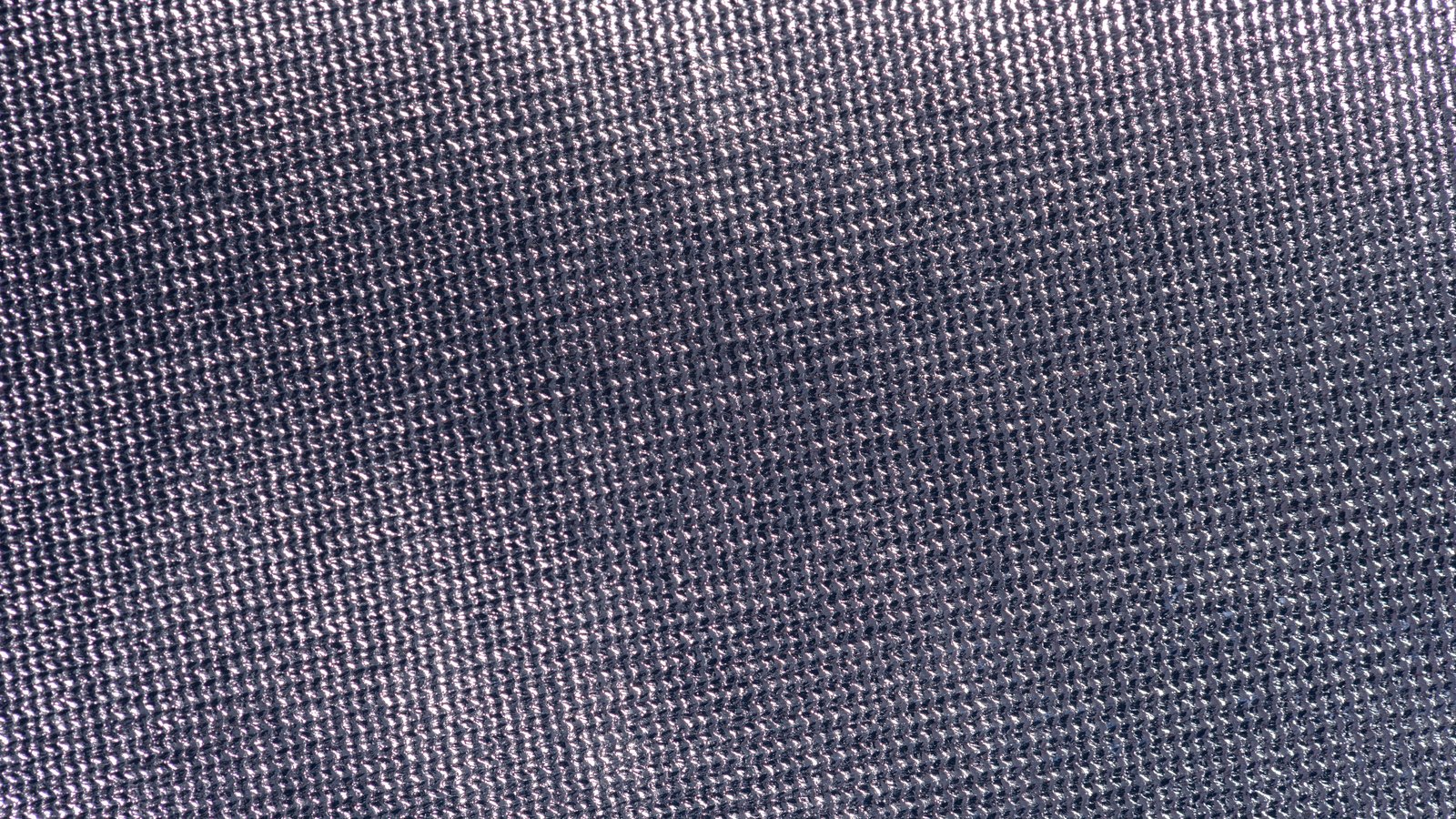 An extreme close view of a fine grey knitted cloth, the small even loops of yarn repeating across the whole frame under a soft raking light that lifts a faint blue sheen from the fibres. No text, brand mark, person, object edge or background is in view.