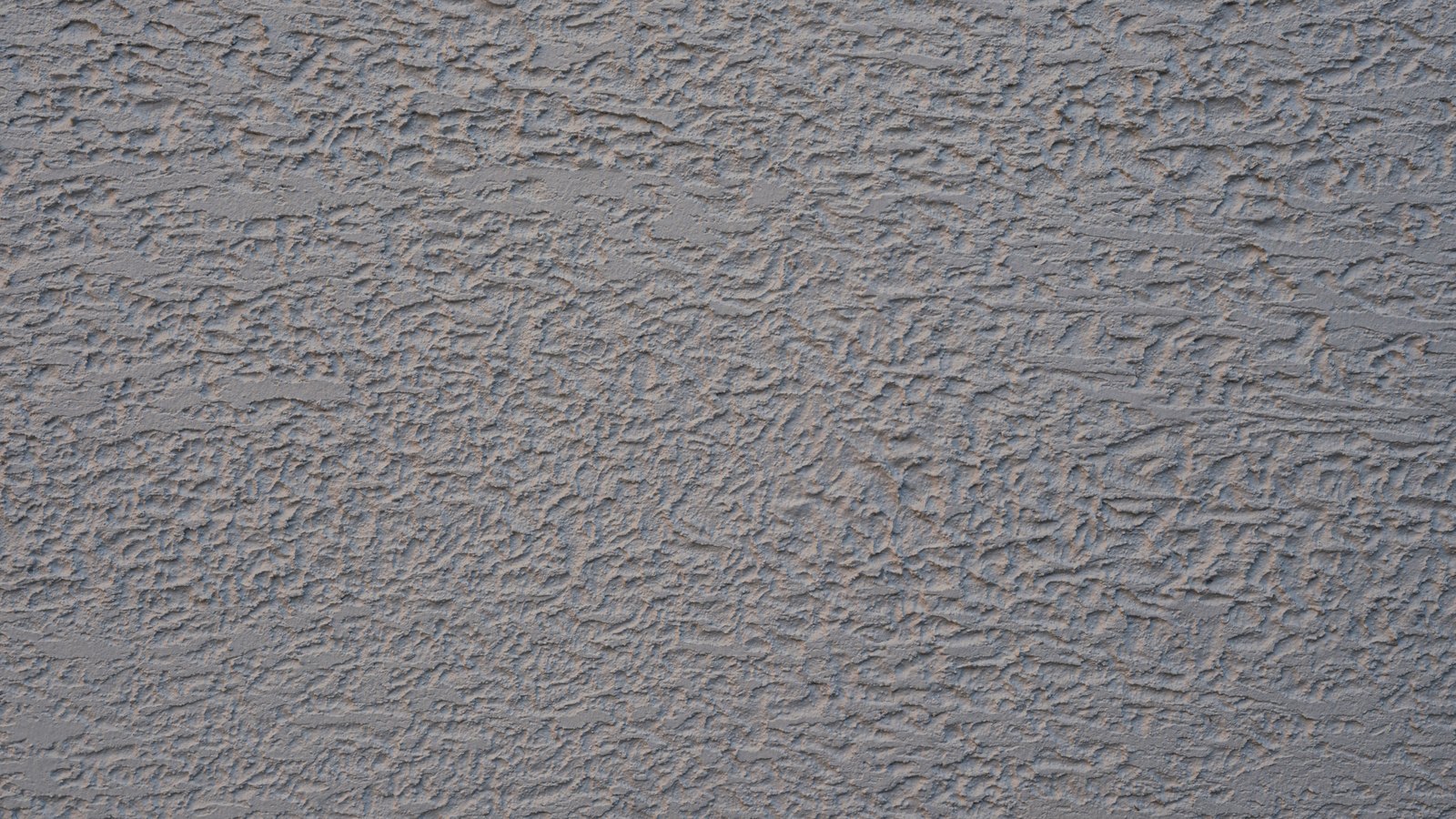 A close photograph of a rendered wall, grey and faintly blue plaster worked into a fine irregular relief that fills the frame from edge to edge. No object, person, lettering or brand mark is visible.