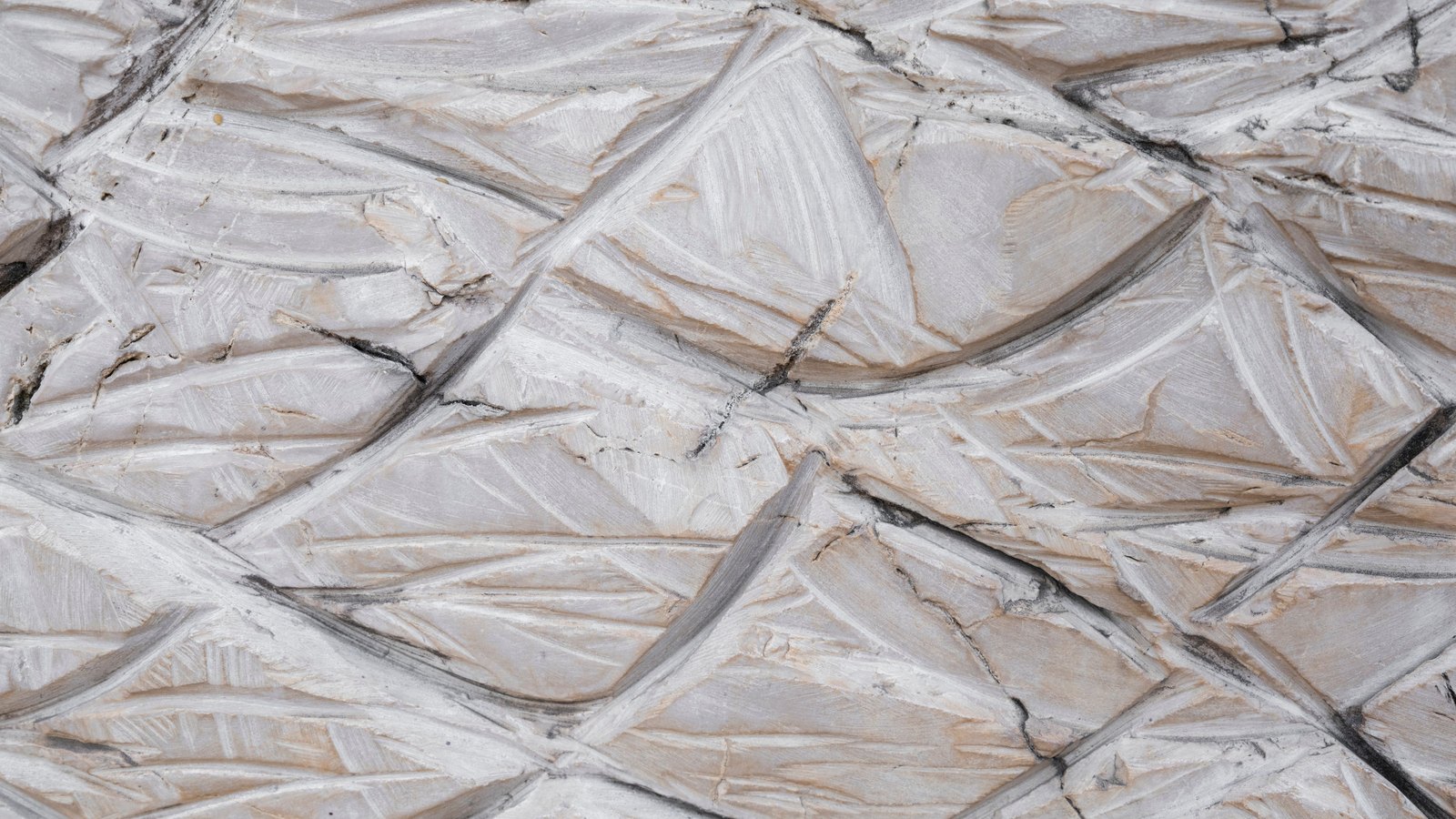 A close crop of a pale grey and cream stone surface cut into angular chiselled facets, with darker fissures running between them and no text, people or buildings in view.