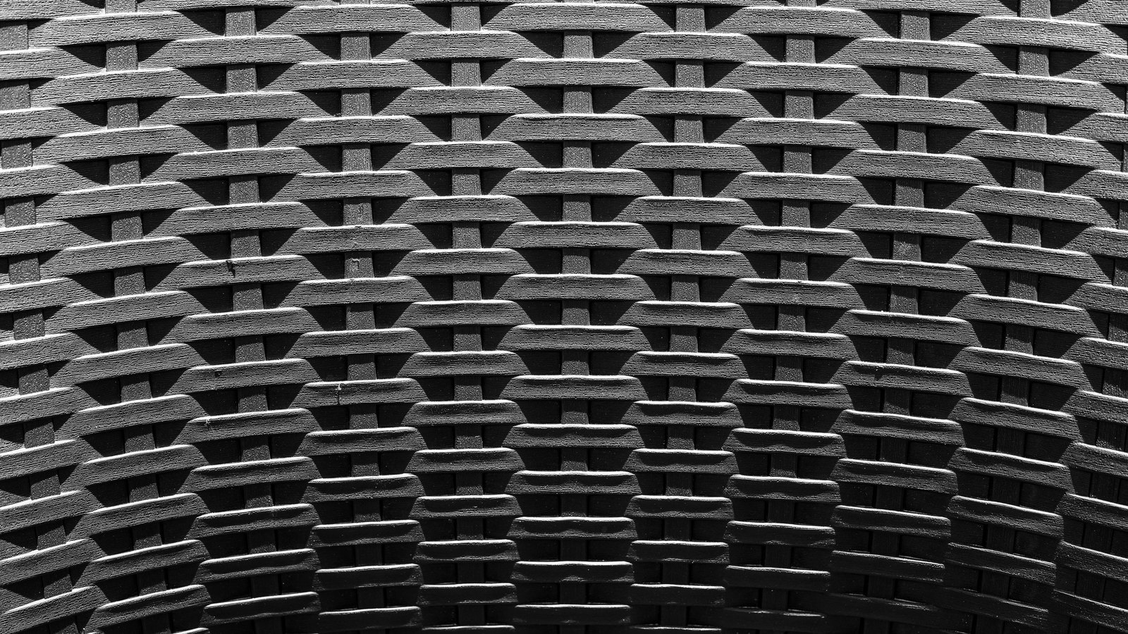 A close monochrome view of a dense basket weave in dark grey synthetic rattan, the interlocking strands repeating in even rows across the whole frame. No text, brand mark, person or horizon is in view.