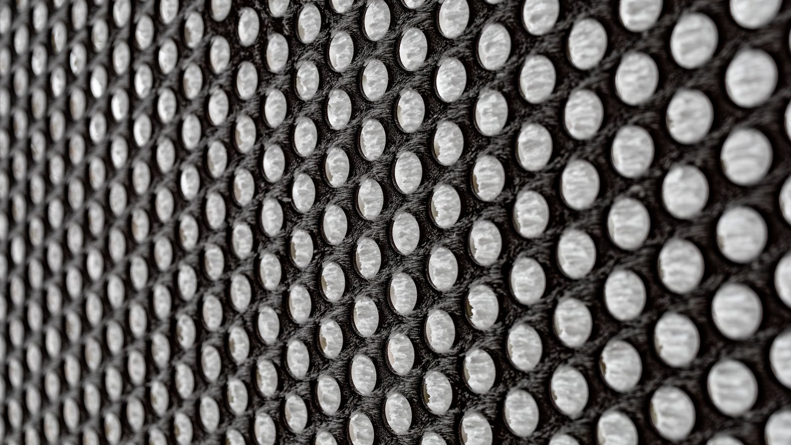 A close photograph of a two-layer spacer mesh, a dark outer grid of evenly spaced oval openings backed by a white inner layer, the rows curving away into shallow focus at the left edge, with no text, marking or object in view.