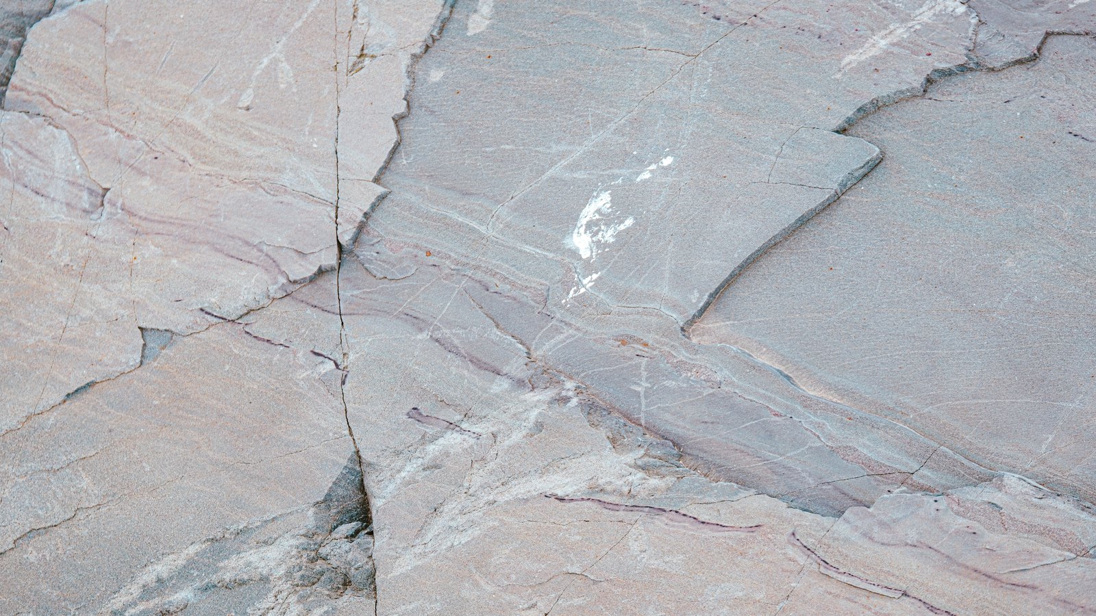 A close photograph of a pale grey and pink rock face, flat layers meeting along a crack that runs from the top of the frame to the bottom and splits the surface in two. No object, person, lettering or brand mark is visible.