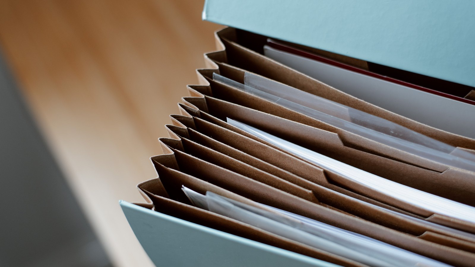 A close-up of an expanding file folder with kraft-brown dividers holding documents on a wooden desk.