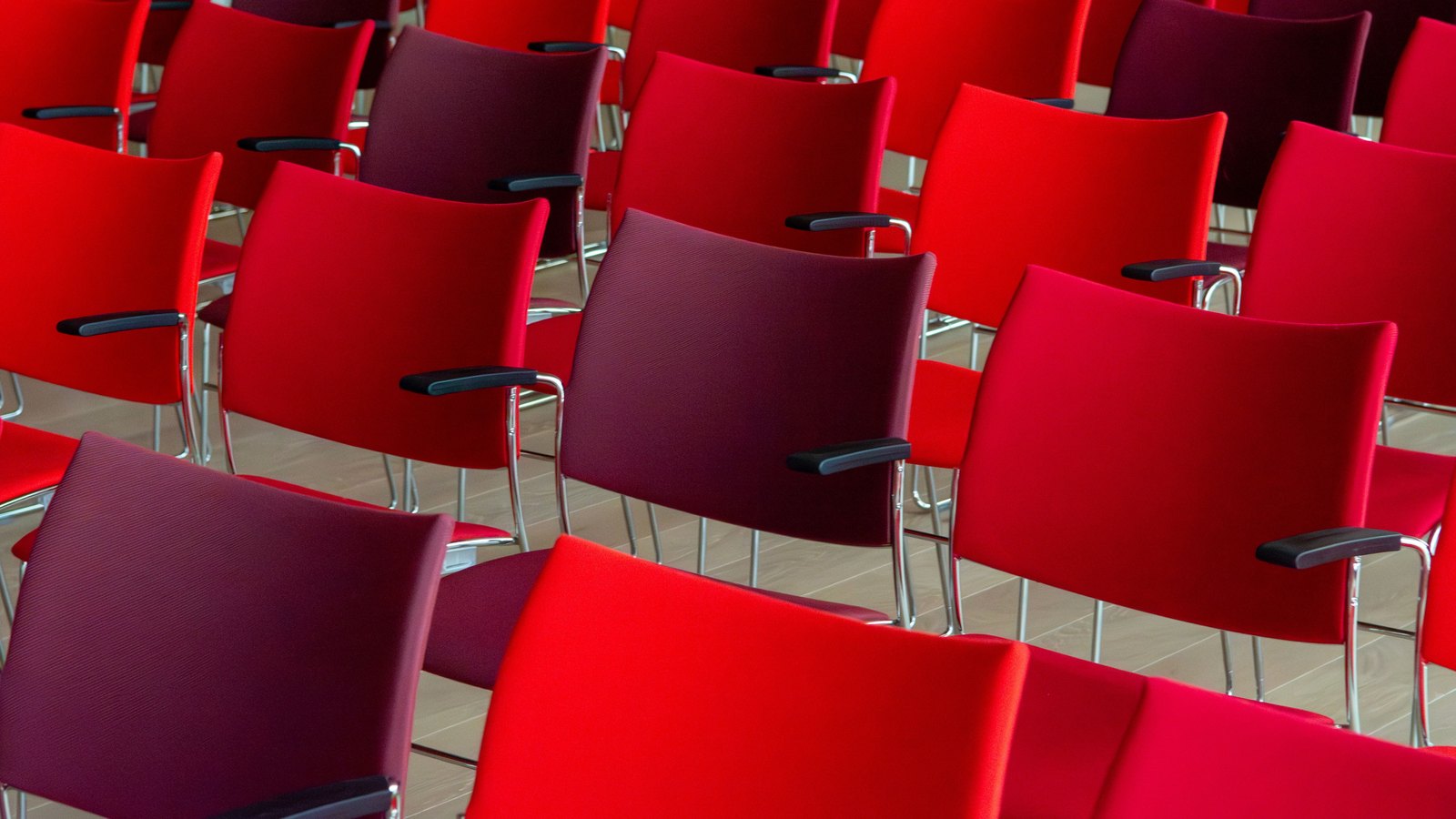 Rows of empty red and burgundy chairs in a meeting room, not a photograph of this event.