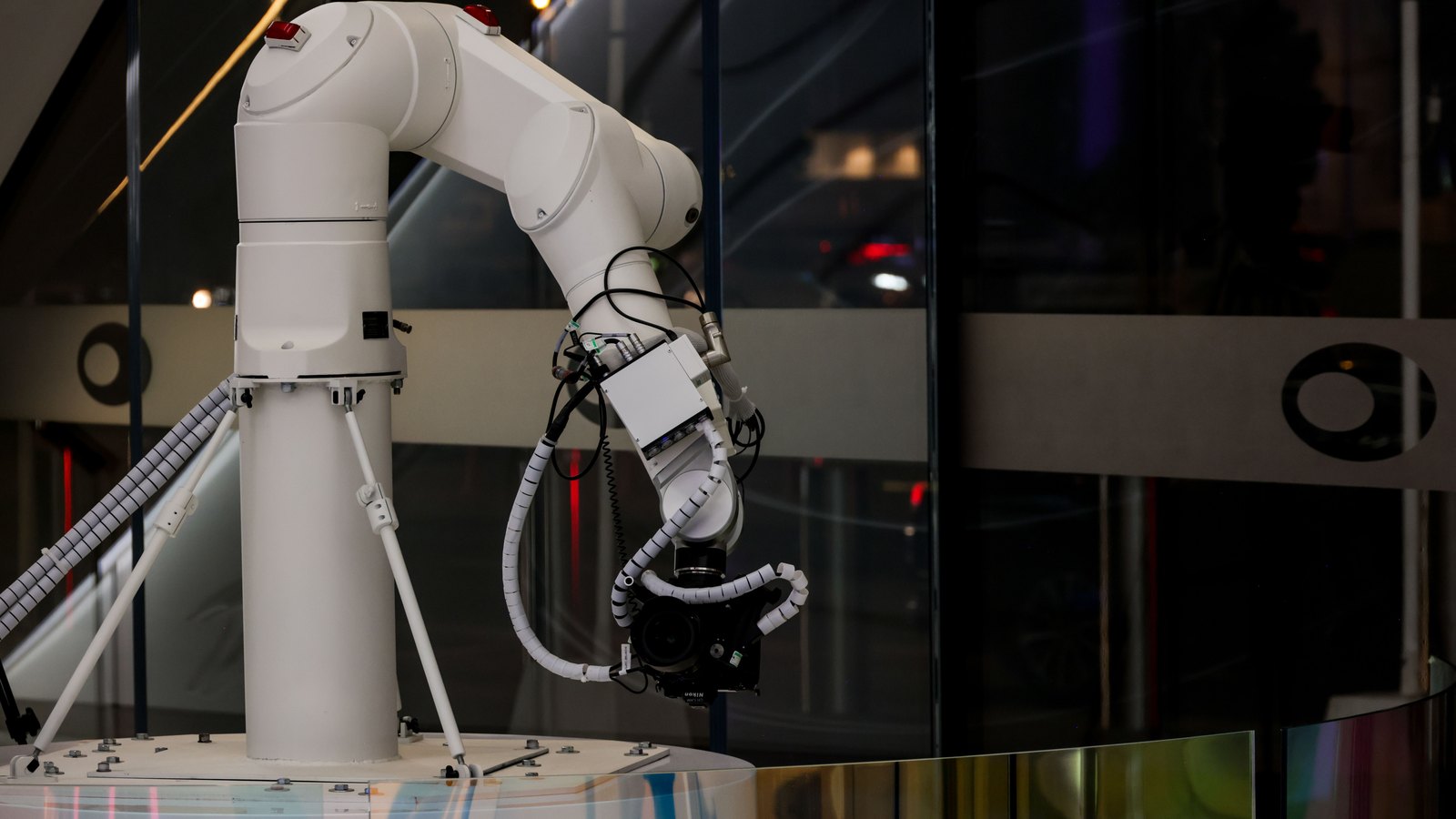 A white industrial robotic arm holds a camera behind glass.