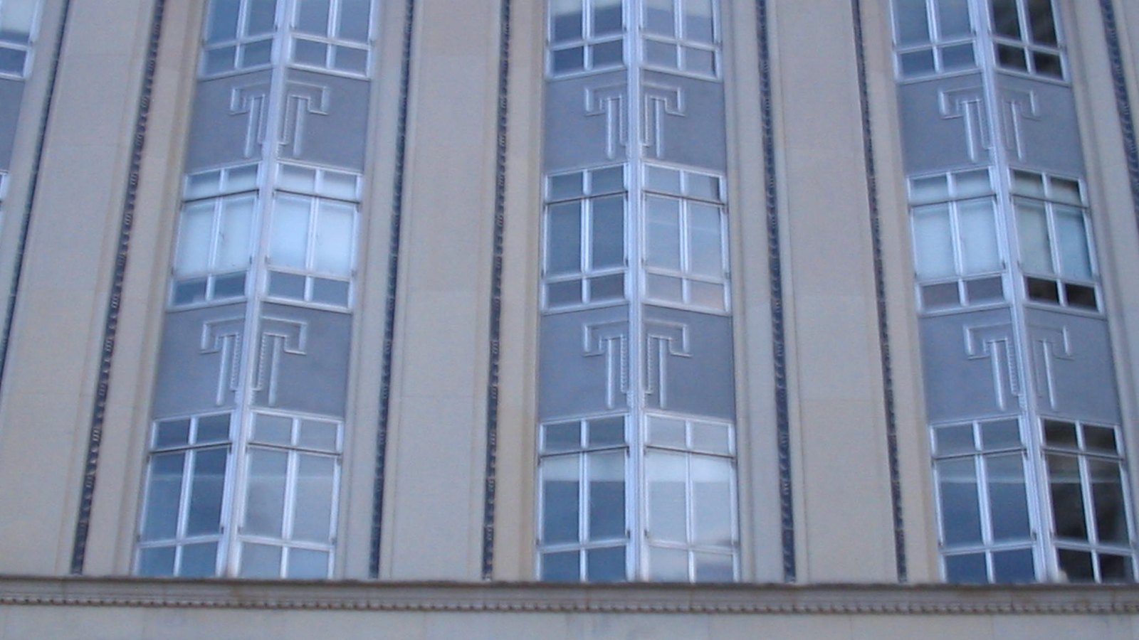 A close view of three tall window bays on the limestone facade of the Eldon B. Mahon United States Courthouse in Fort Worth, each bay set between fluted piers and carrying a repeated stepped Art Deco relief in the stonework between the upper and lower windows.