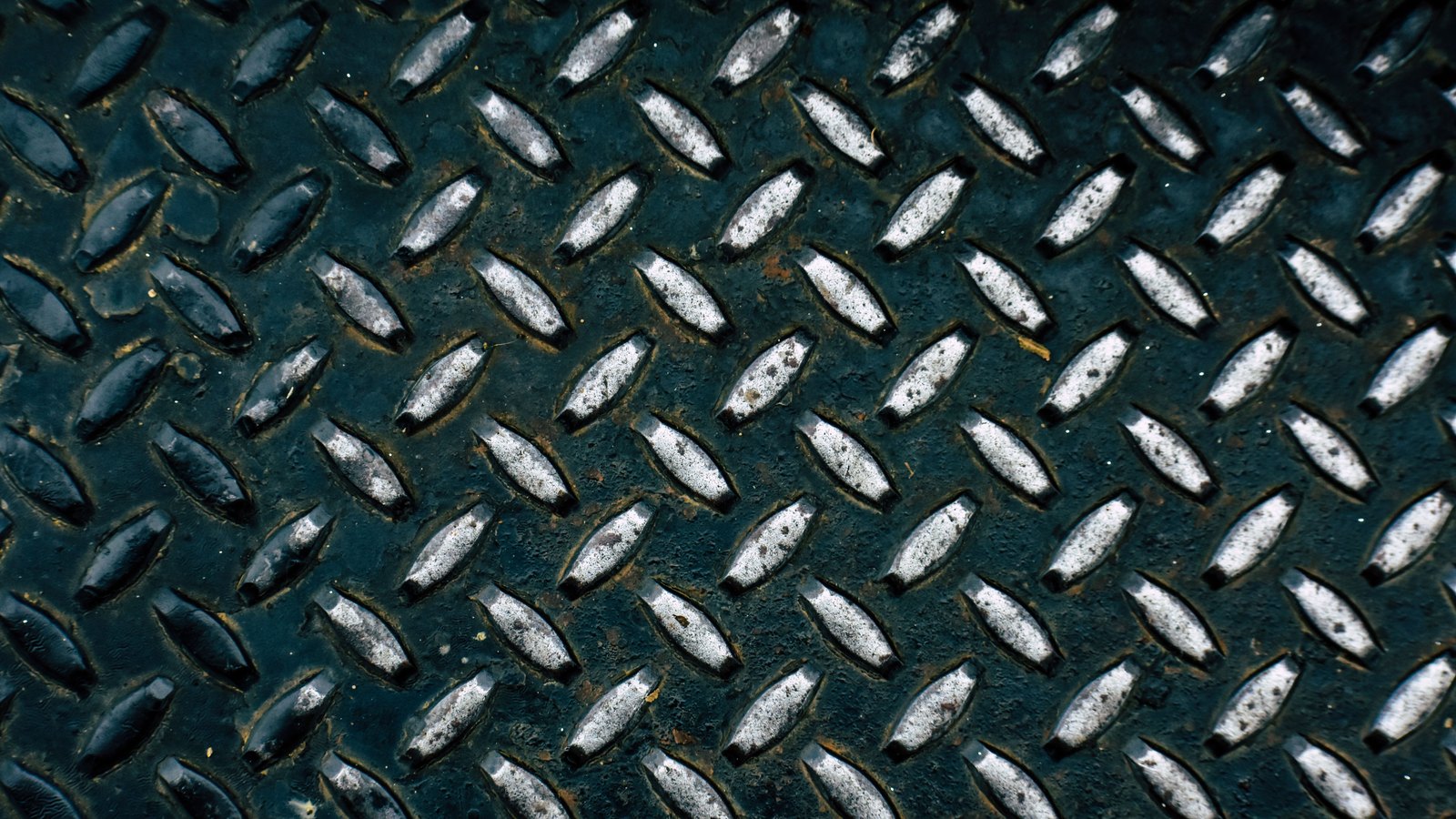 A close-up of dark teal steel chequer plate, its raised diamond treads catching the light in regular diagonal rows.