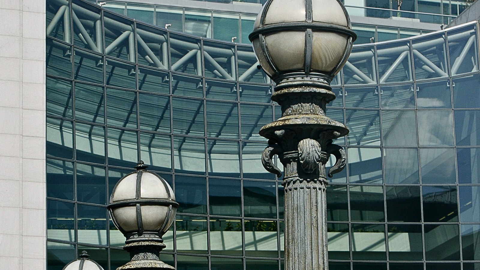 The curved glass curtain wall of the Securities and Exchange Commission headquarters in Washington, its exposed steel bracing visible behind the glazing, framed by two ornamental cast iron lamp posts with globe lanterns.