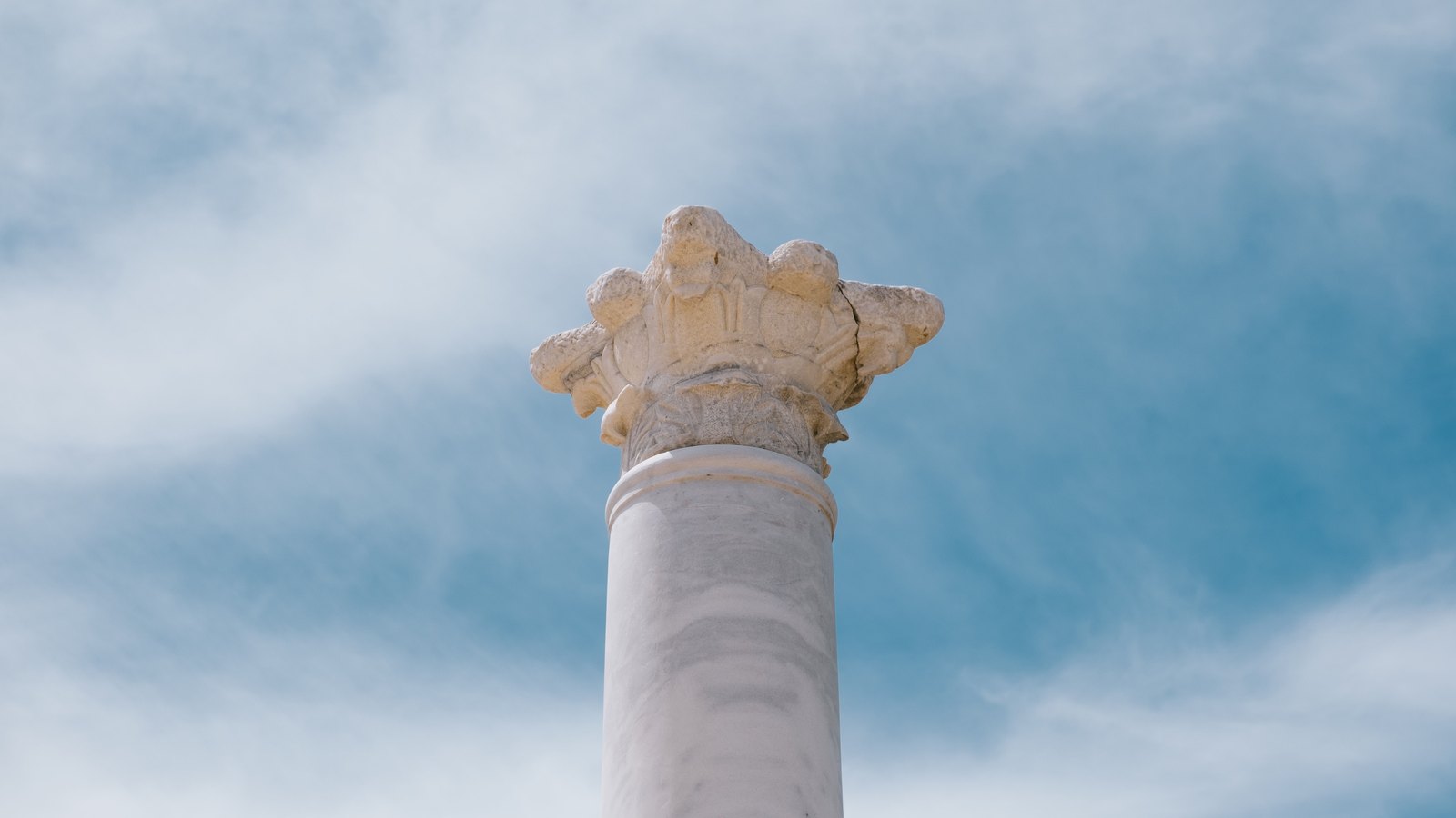 A white marble column rising against a cloudy blue sky.