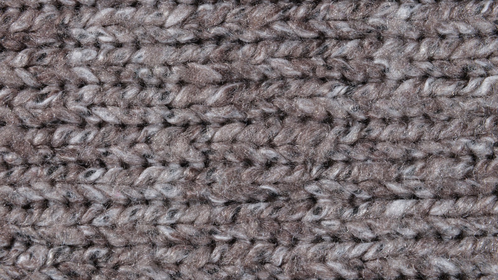 A close photograph of a heavy knitted wool fabric in grey and brown, rows of thick chain stitch running horizontally across the whole frame with loose fibres catching the light. No object, person, lettering or brand mark is visible.