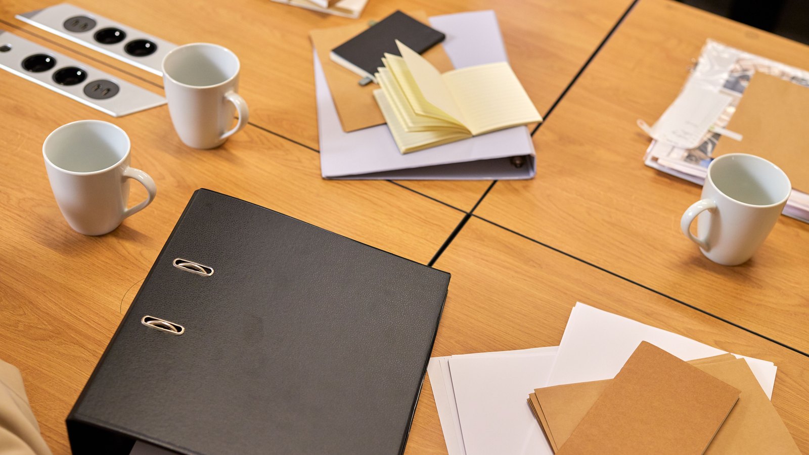 Black binders, notebooks and loose papers arranged on an empty conference table.
