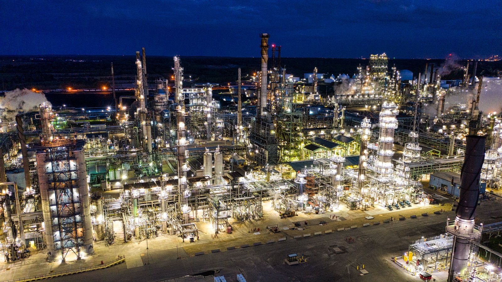 An illuminated oil refinery spreads across an industrial site at night.