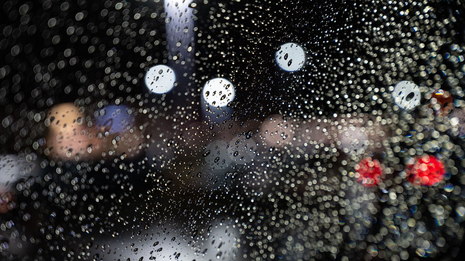 Raindrops cover a windshield while traffic and streetlights blur beyond it, not a photograph of Wednesday's storms.