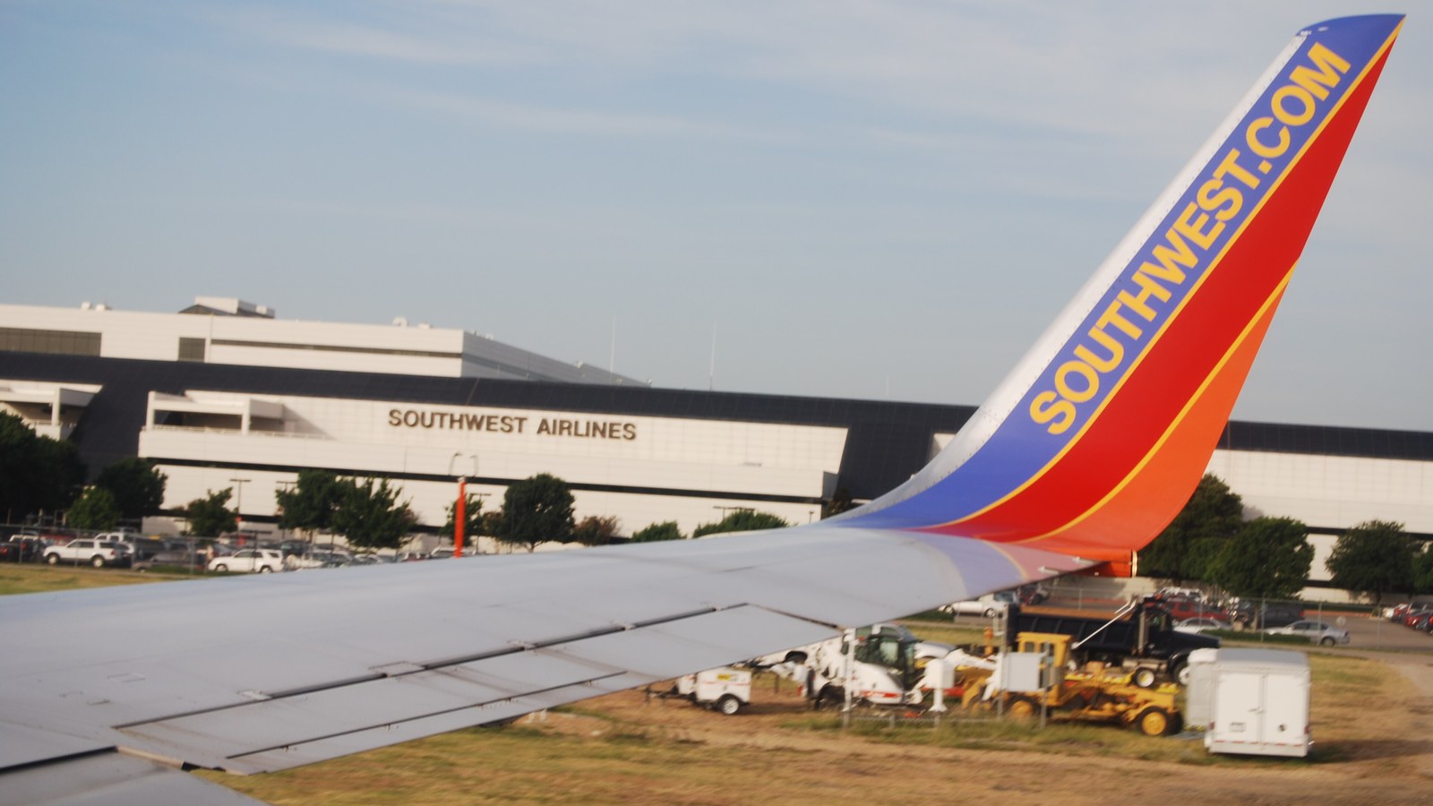 The blue, red and orange winglet of a Southwest Airlines jet seen from a passenger window, with the Southwest Airlines headquarters building at Dallas Love Field behind it.