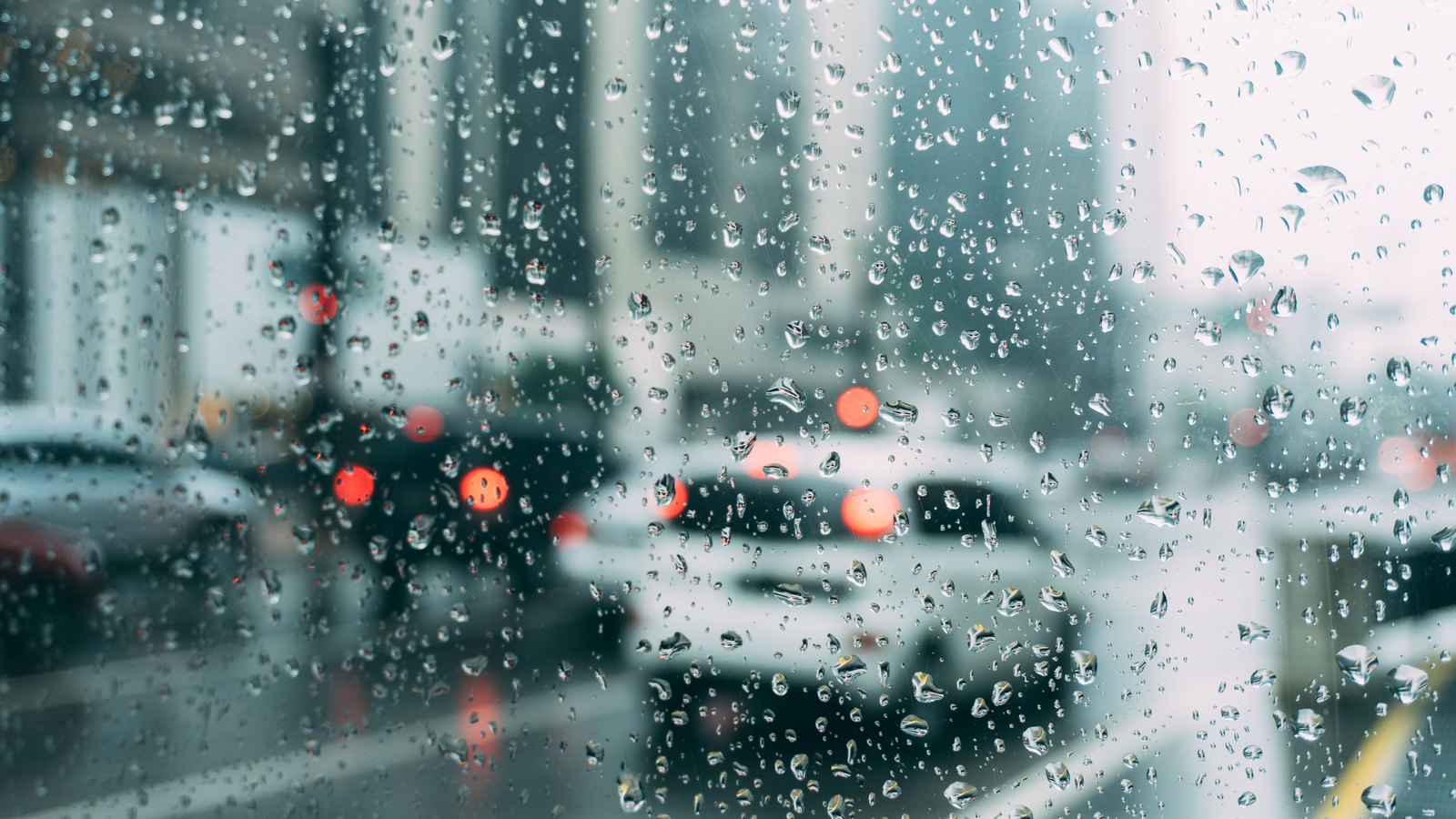 Rain beads on glass while cars and red brake lights blur beyond it, not a photograph of this advisory.