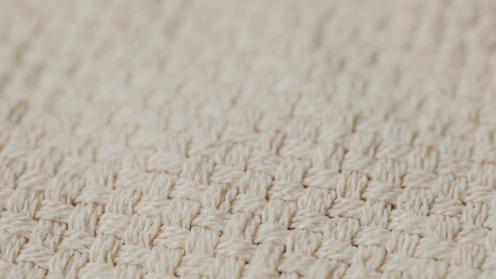 A close view of a pale knitted textile, its loops running in even rows across the whole frame.