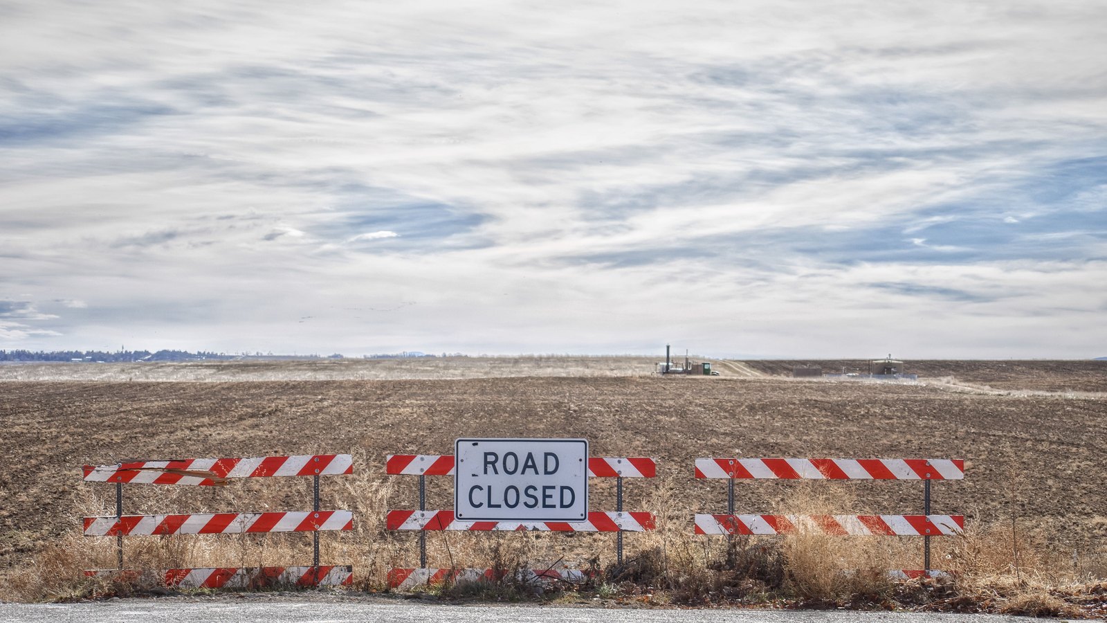 A road closed barricade sign standing across an empty road.