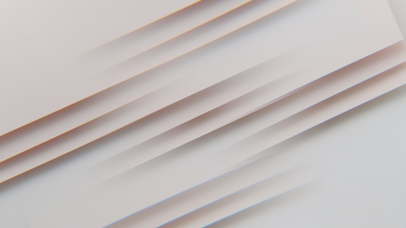 Several sheets of pale card laid across each other at a slight angle on a light surface, each edge casting a thin soft shadow on the sheet below.